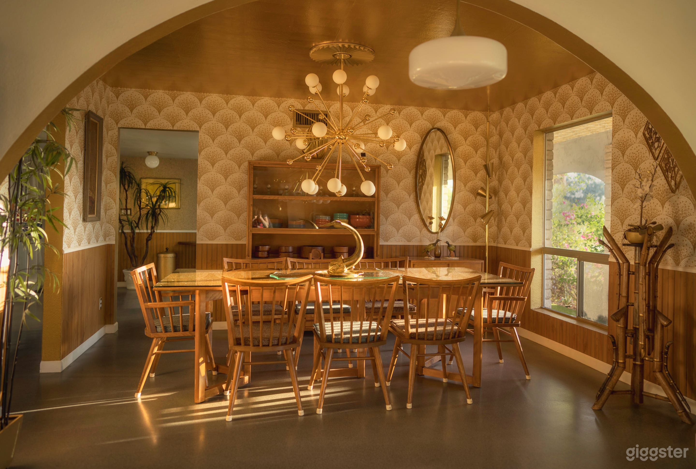 The main house’s midcentury dining room has a full 1950s Conant Ball set: table, chairs, &amp; hutch—beneath a starburst chandelier and gold leaf ceiling. Warm wood paneling, scalloped wallpaper, &amp; vintage dinnerware complete this glowing atomic-era room.