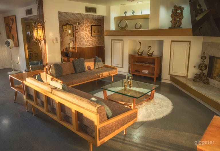  The midcentury living room features custom wood-frame sofas, concrete floors, 1950s Conant Ball furniture, &amp; a golden fireplace. Sunlight pours in onto rich textures, atomic accents, and curated art—ideal for retro scenes, lounge setups, and period filming 