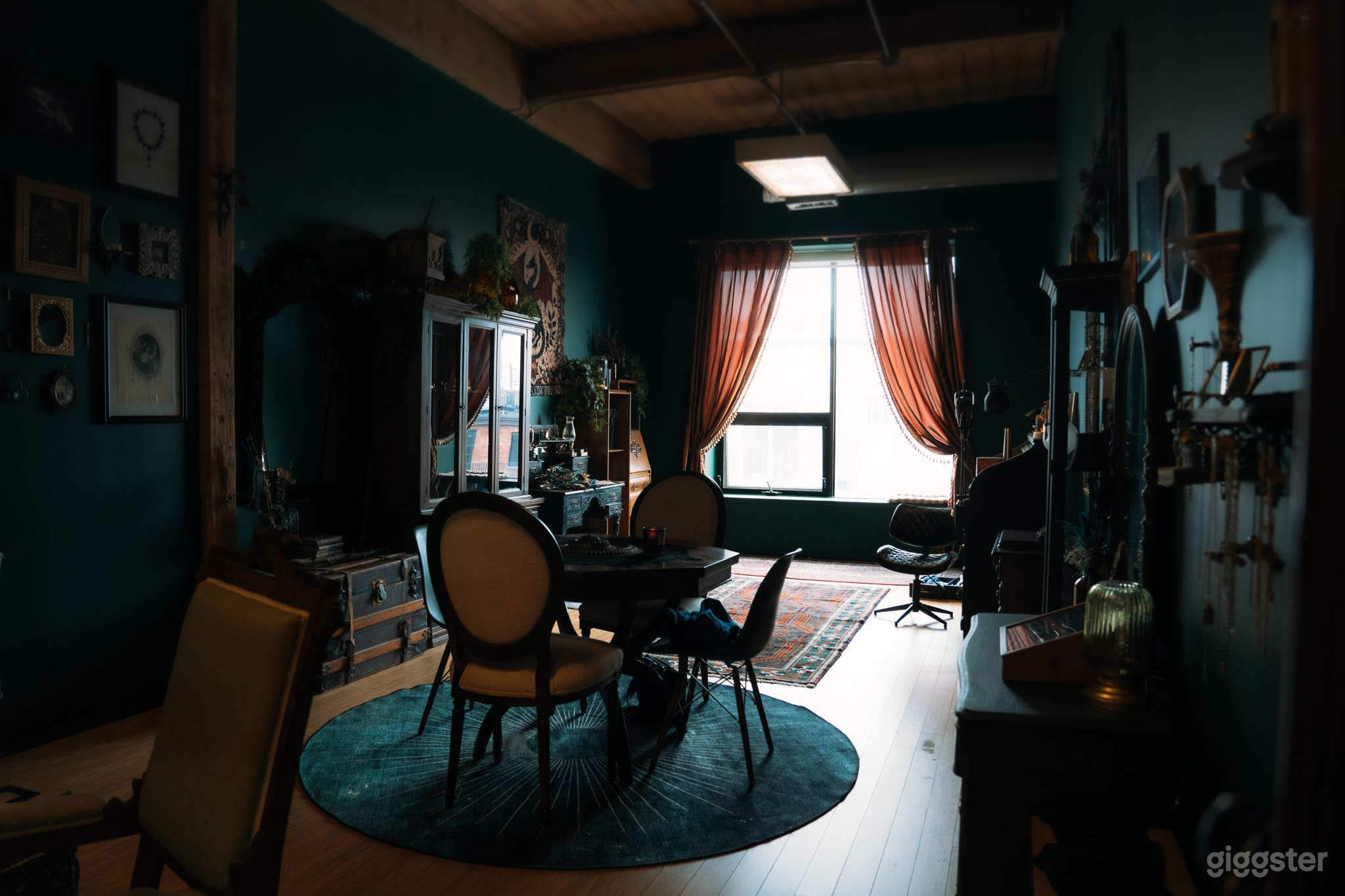 View from the door. Large window lets in lots of natural light in the back half of the room. Ceiling lights (aka big lights) and warm-toned lamps throughout the space.