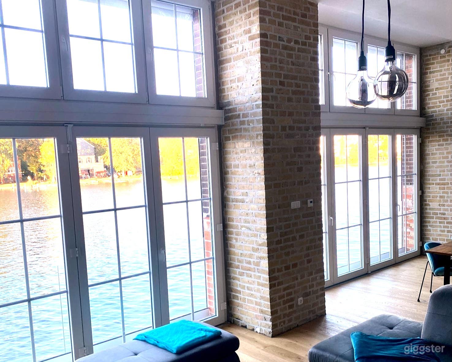 Helles Industrie-Loft direkt am Wasser mit bodentiefen Fenstern, freiliegenden Backsteinwänden und natürlichem Eichenboden — perfektes Licht für Fotoshootings, Veranstaltungen und kreative Produktionen.