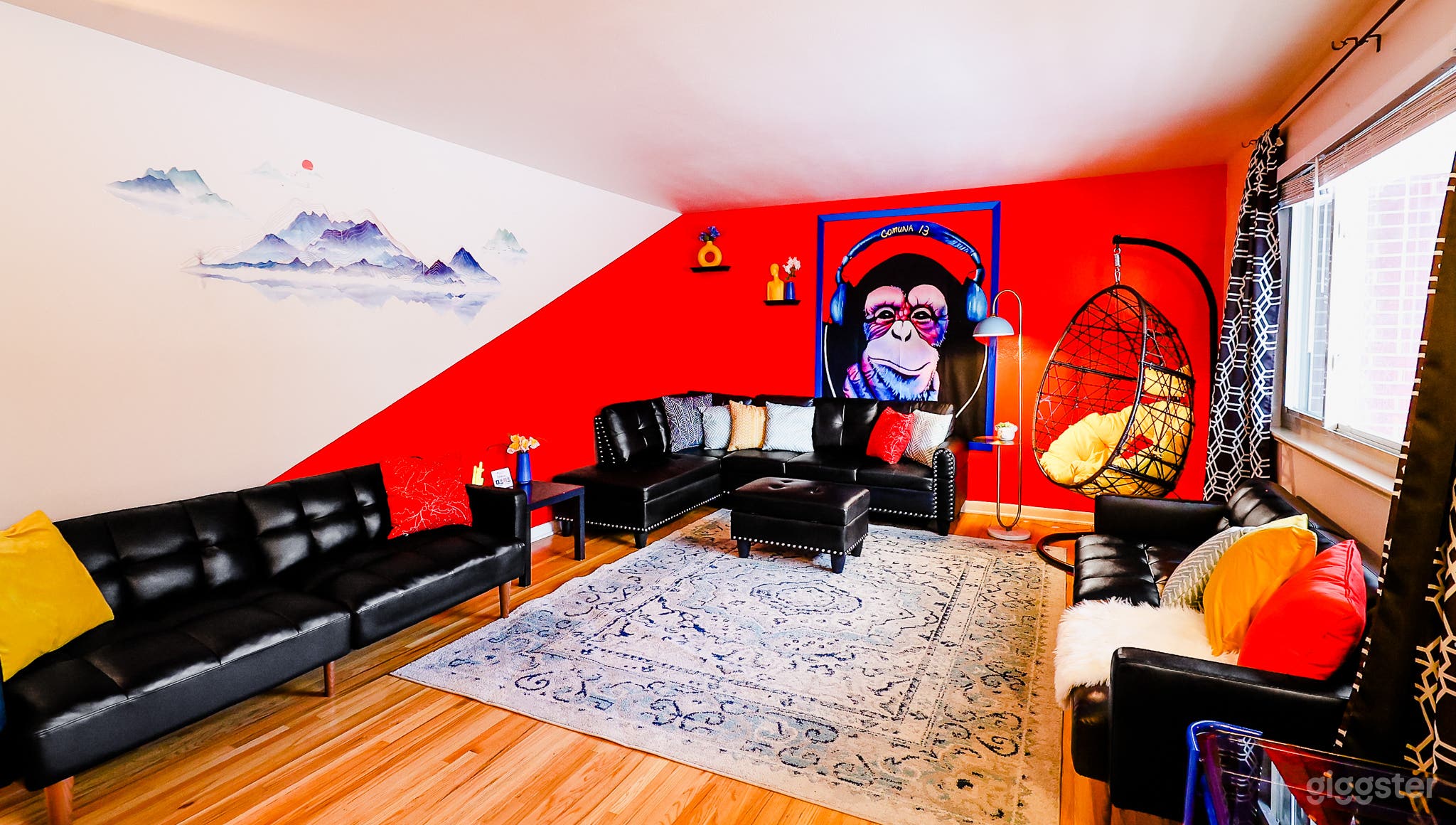 A spacious living room with a striking red and white wall, adorned with a money tapestry, and furnished with a sleek black couch, creating a bold and inviting space.
