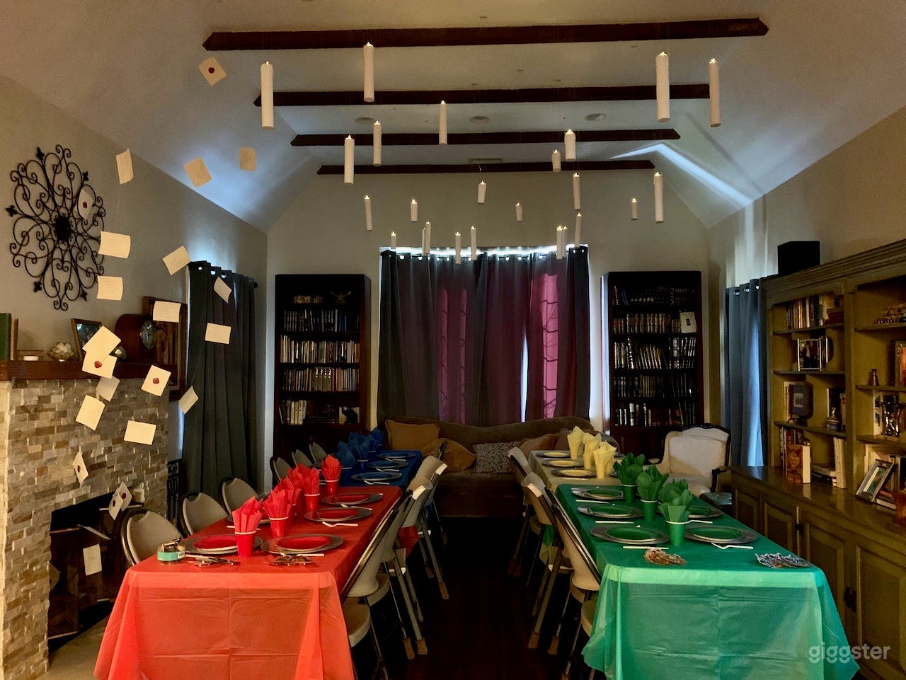 Living room with very high ceilings with inlaid beams, fireplace, bay window showing lush greenery.