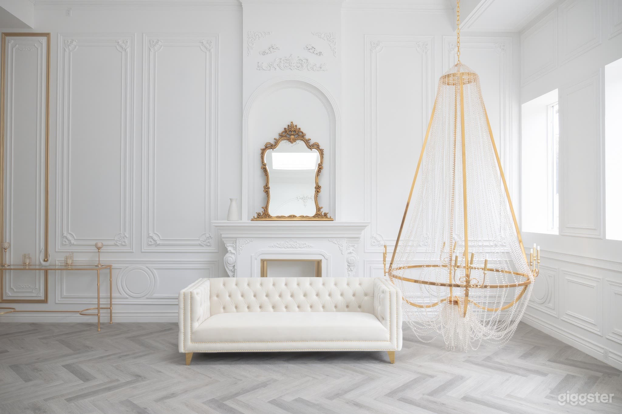 Venetian inspired elegant studio space with a 12ft chandelier, white velvet sofa, antique mirror, grand fireplace, and herringbone floor