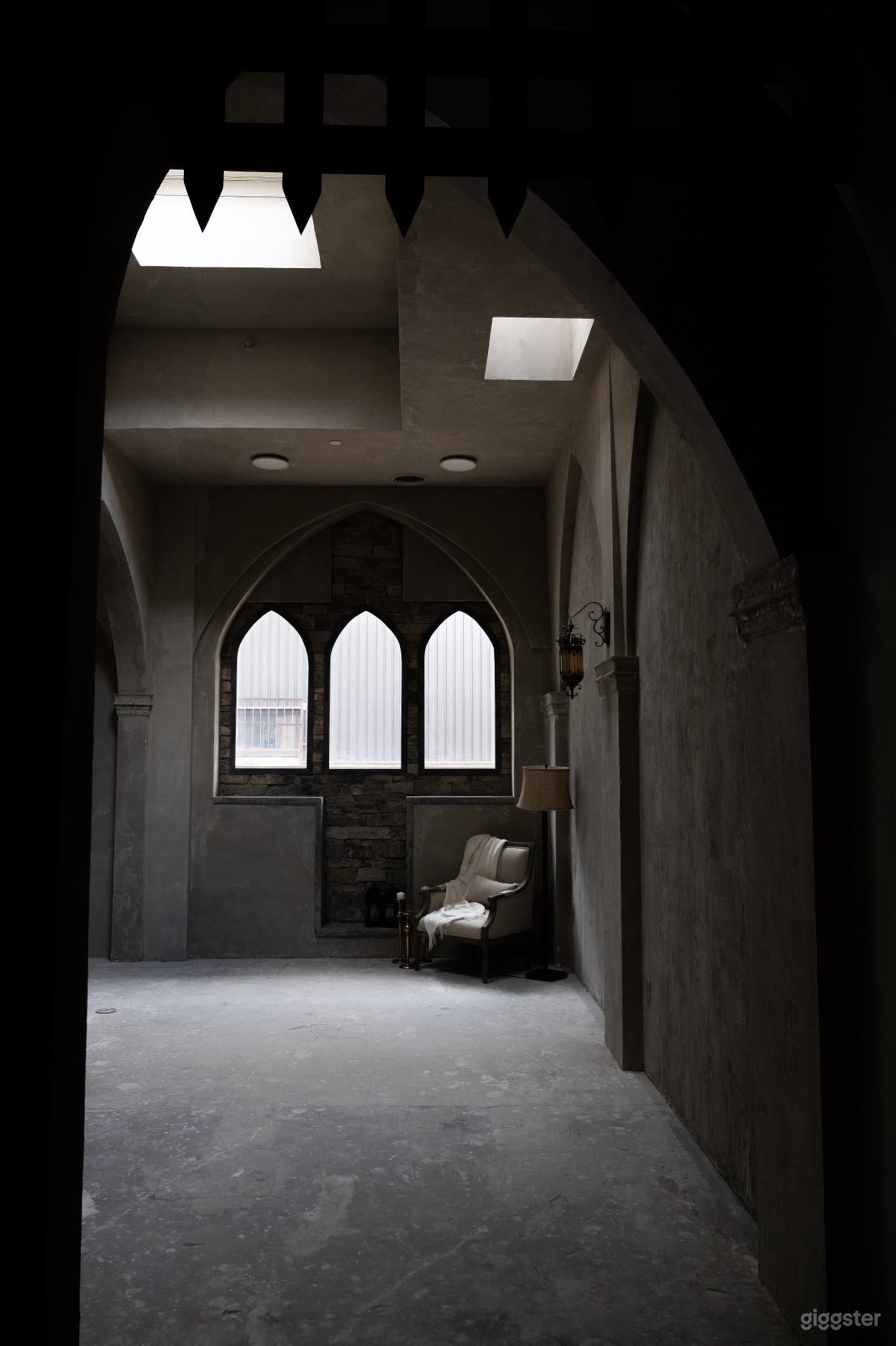 Medieval studio room featuring three cathedral windows, period-inspired furniture, and gray plastered walls, adding authentic medieval ambiance.