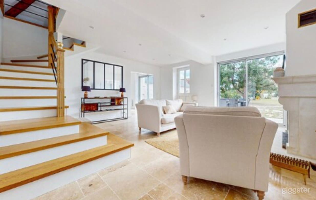 Salon autour d’une cheminée en pierres menant au 1 er étage via un large escalier en bois 