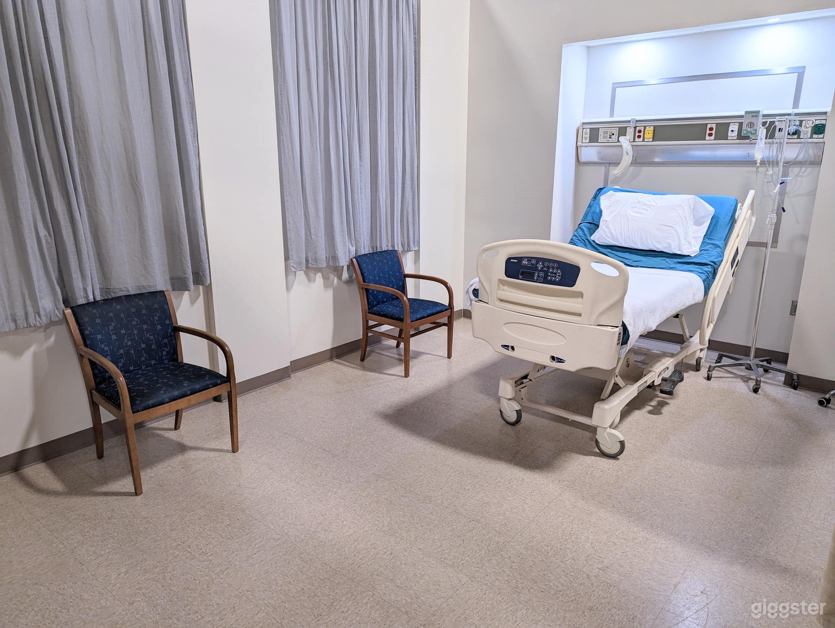 The large patient room has working medical equipment: a working bed, working IV pole with fluids and IV line, vital signs monitor, etc