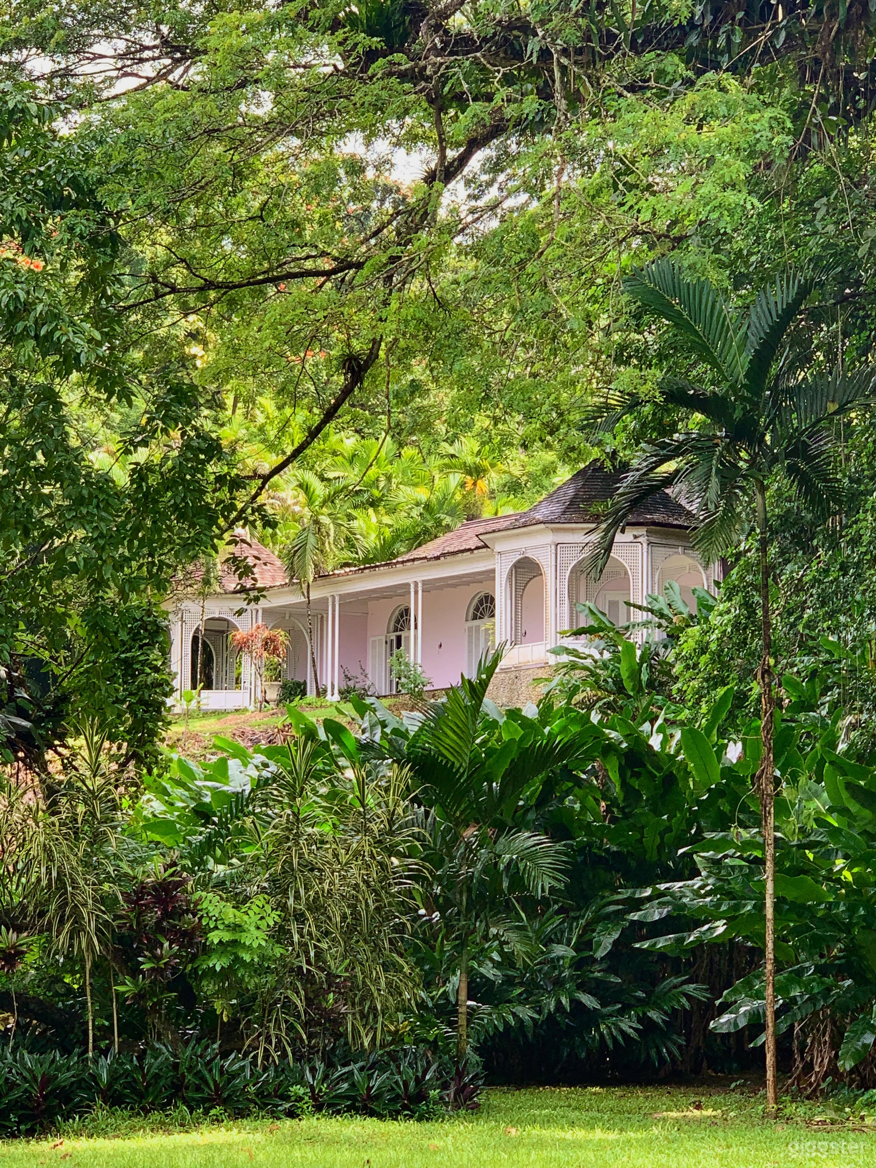 Charming 1950s villa framed by tropical greenery — the wraparound veranda and colonial arches provide a timeless, cinematic façade ideal for vintage or Caribbean-themed shoots.