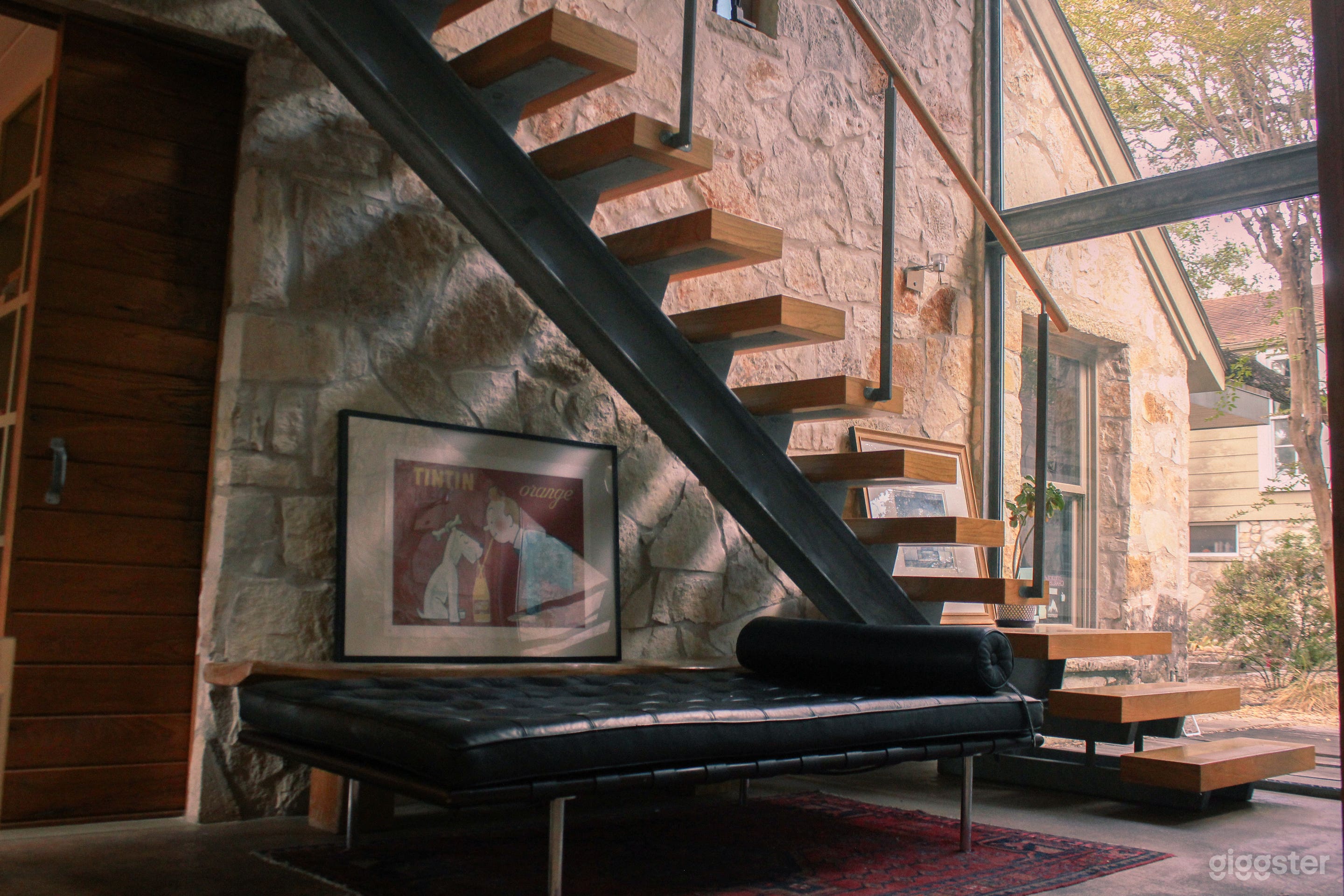Floor to ceiling windows, stone walls, mid-century modern decor, exposed floating staircase, wood and steel