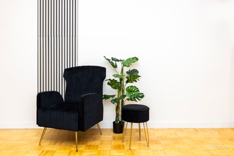 A close-up of the black velvet sofa and a matching footstool, with a monstera plant, against a wall with vertical stripes, showcasing a chic waiting or resting area. 