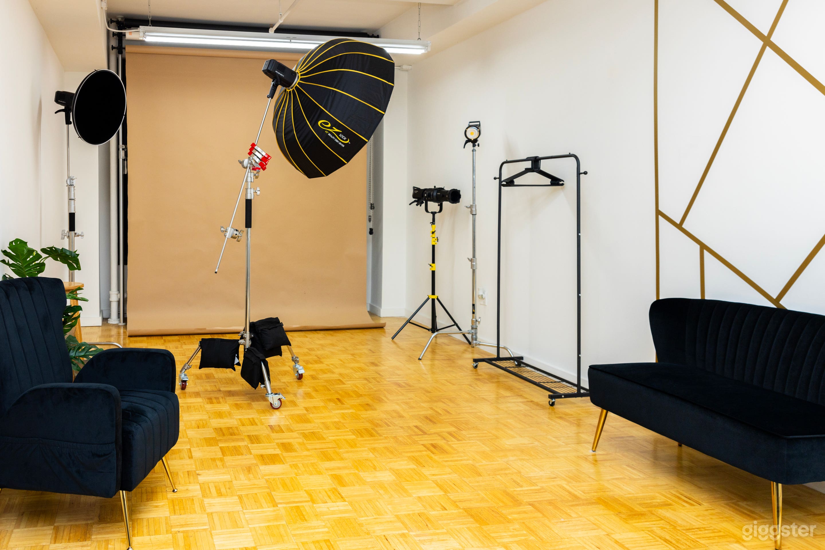 A photography studio setup with a black sofa, a large octagonal softbox, a boom stand, and various lighting equipment against a wall with a geometric golden pattern.