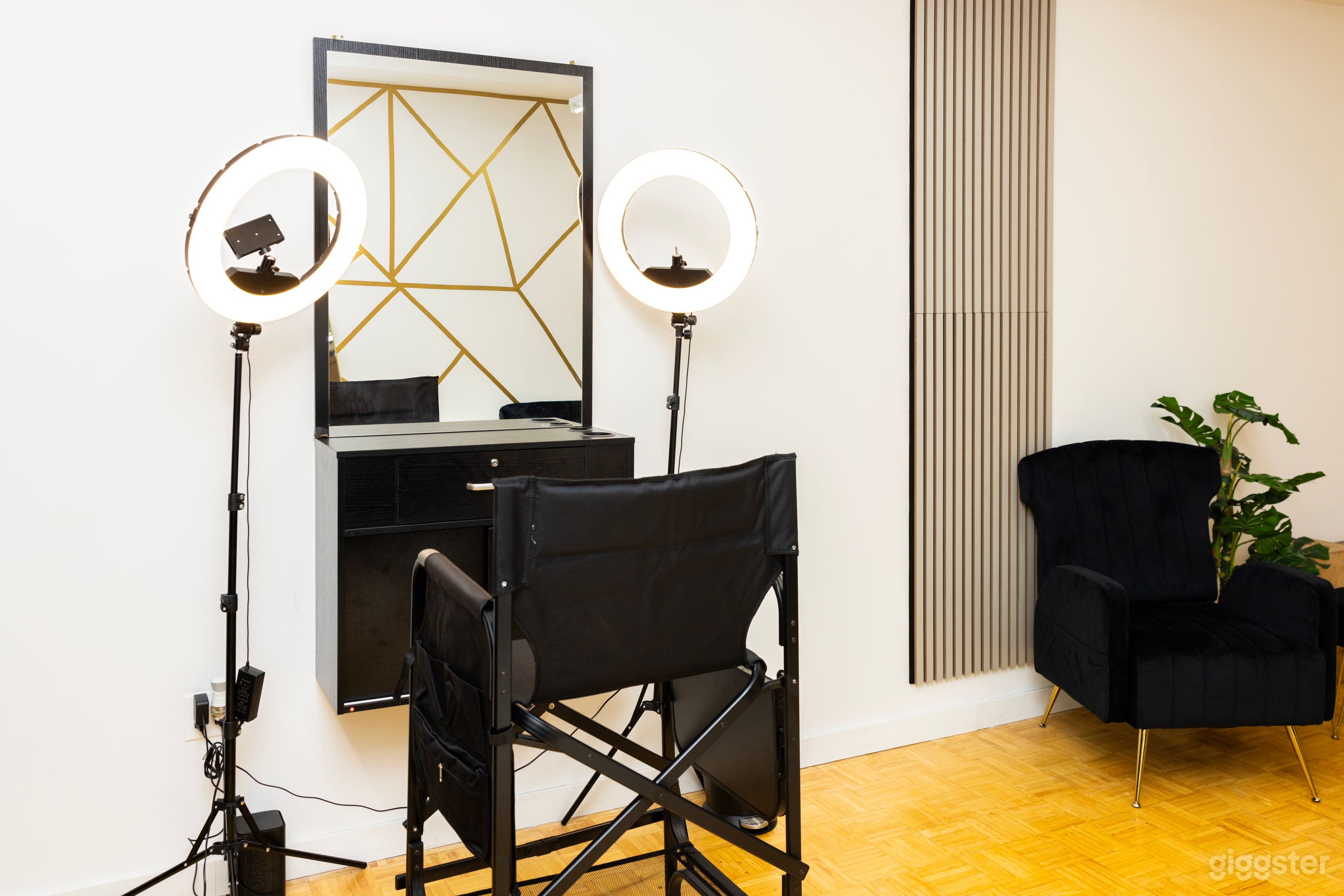 Another angle of the photography studio showing a director’s chair positioned in front of a vanity mirror with ring lights, with a black sofa and a plant to the side.