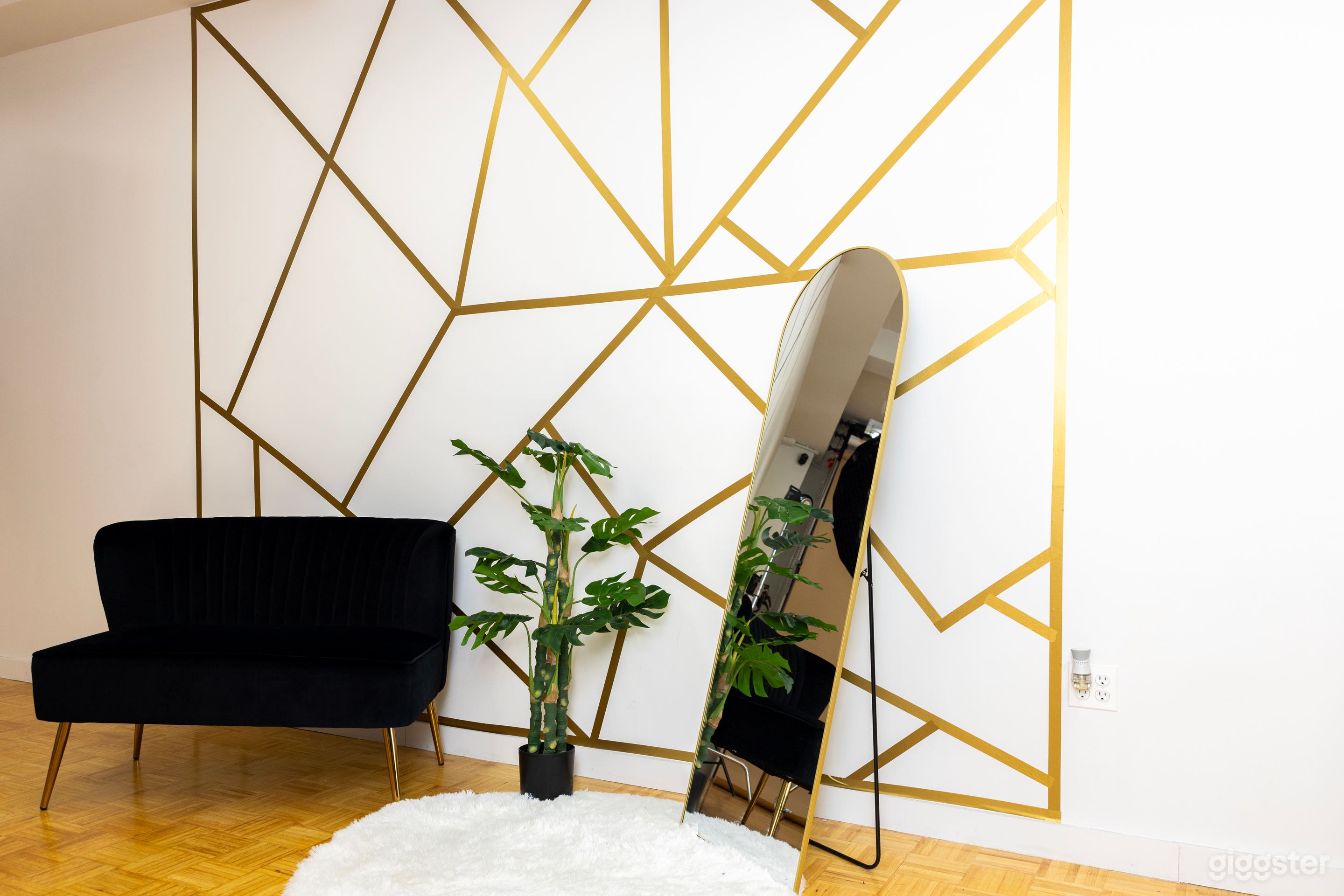 The same corner as the previous image, now with a tall potted plant beside the sofa and the round mirror reflecting the studio lights.