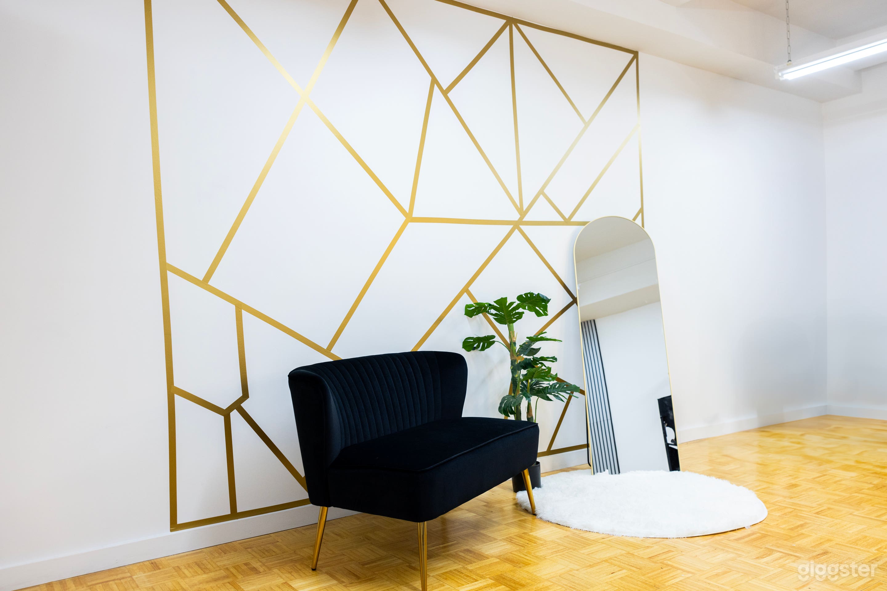 A minimalist corner featuring a black velvet sofa, a round mirror leaning against a geometric-patterned wall, and a fluffy white rug on the wooden floor.
