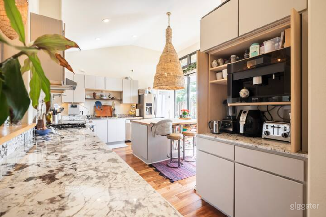 Wide shot of the open-concept gourmet kitchen featuring a marble countertop, large island, and integrated coffee and appliance station. Bright natural light and clean modern design make it ideal for cooking segments, lifestyle shoots, or product-focused film work.