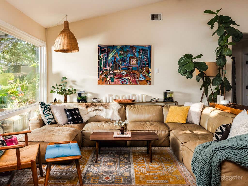 Spacious Boho-meets–rock-and-roll living room featuring a raw leather sectional, vintage furnishings, and original artwork by surrealist artist Barbara Romain. Natural light, bold textures, and creative energy make it perfect for film, photo, or lifestyle shoots with a warm, artistic vibe.