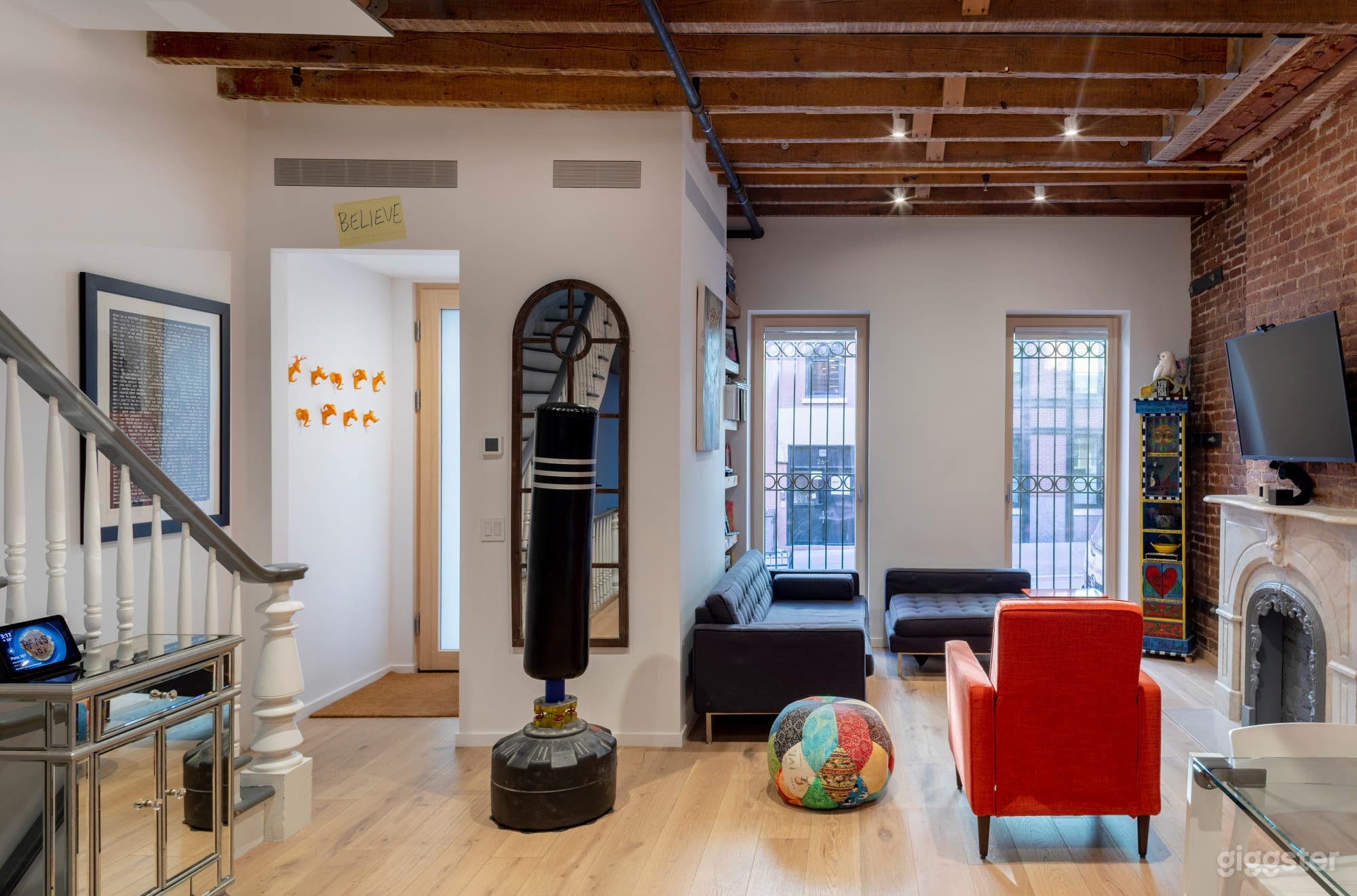 Living room with large windows, fireplace, large beam hardwood floors, exposed beams in ceiling, exposed brick