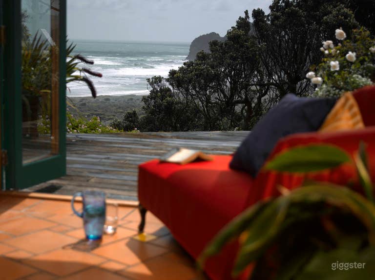  Cabaña Te Koinga con puertas plegables hacia la gran terraza de madera y comedor al aire libre con barbacoa de leña con vista a la Playa Bethells. 
