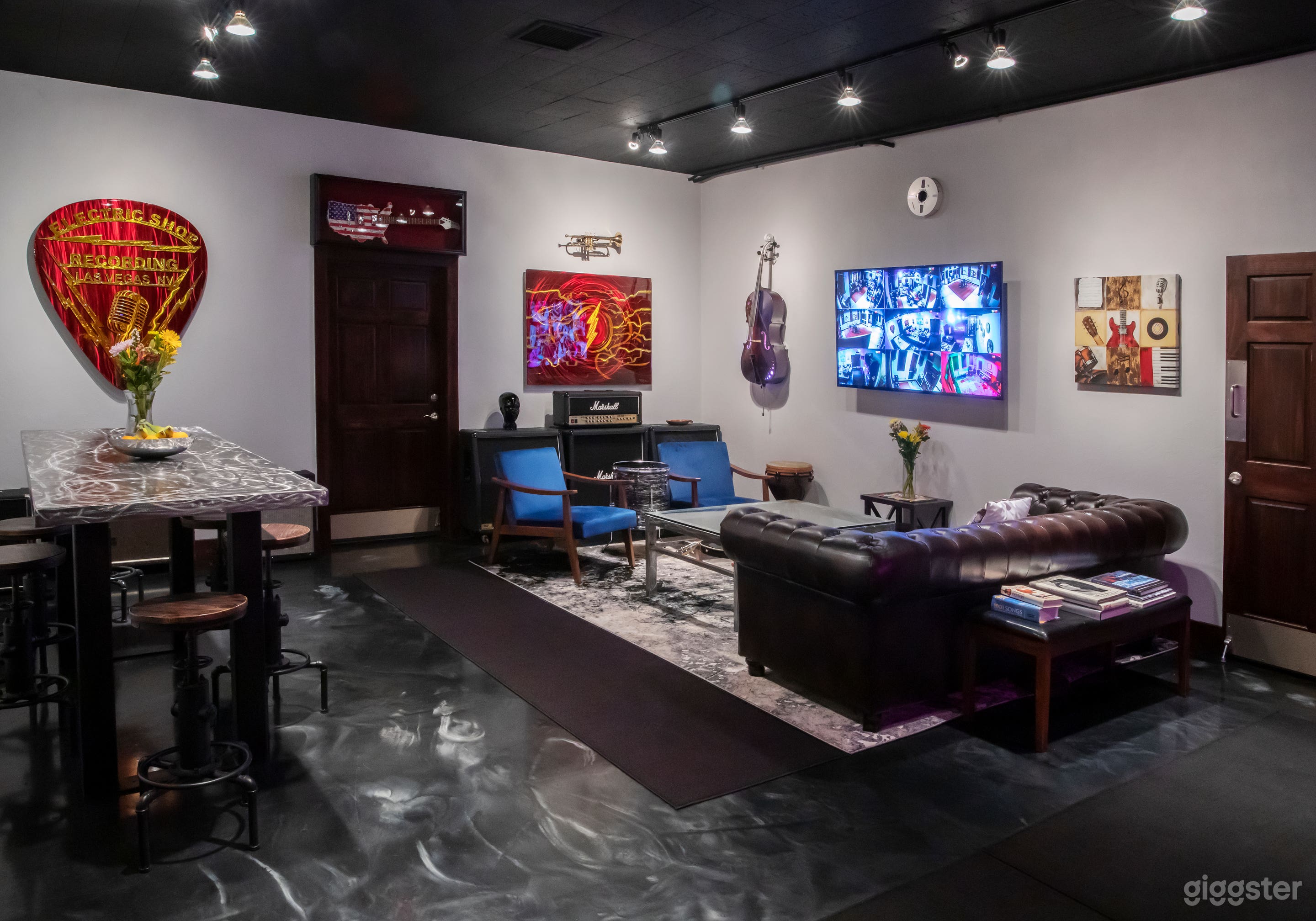 Left side Break room and lounge area has a couch with a glass guitar coffee table, 2 arm chairs, a conference or dining table with 6 adjustable stools, a kitchenette and music themed art.