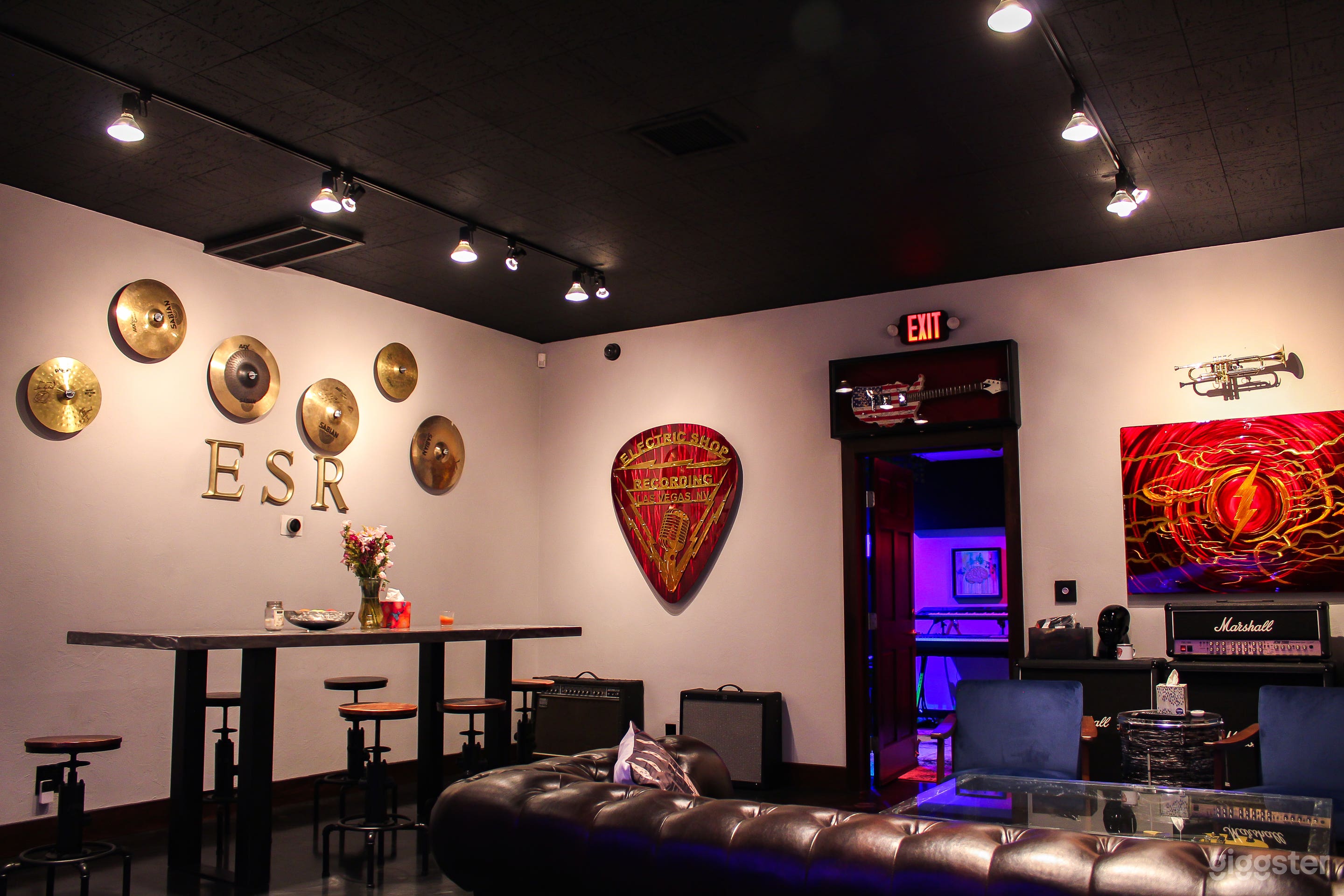 Right side Break room and lounge area has a couch with a glass guitar coffee table, 2 arm chairs, a conference or dining table with 6 adjustable stools, a kitchenette and music themed art.