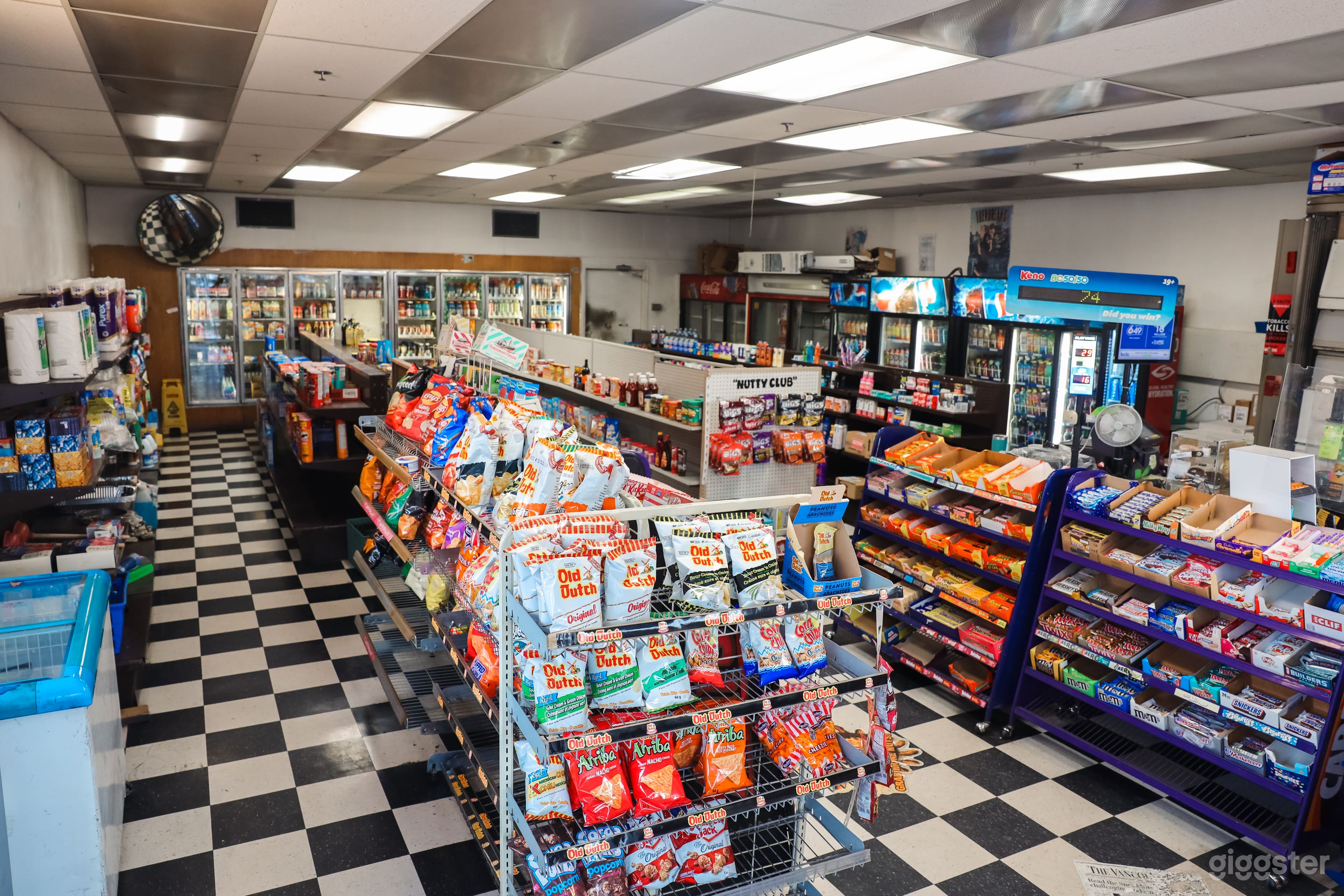 View of the inside of the store. has 3 aisles with grocery products. Also, there is a door that leads to the back of the store which contains storage and  shelving.
