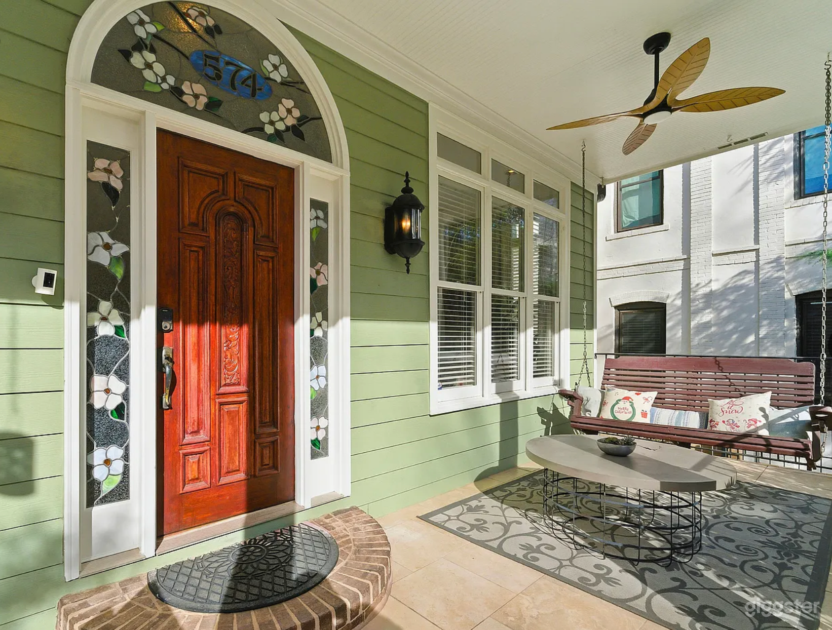 Oversized porch with conversation seating, porch swing, custom stained glass arched windows, and carved front wood door
